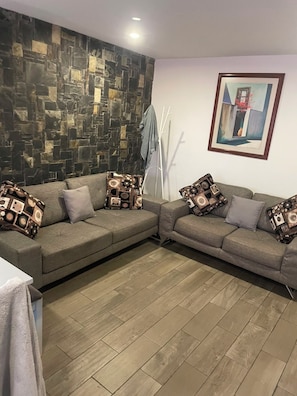 Sala de estar com dois sofás, almofadas estampadas, parede de pedra, um quadro e piso de madeira.