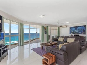 A spacious living room with a large window overlooking the sea, a sofa set, and a flat-screen TV. - Burleigh Surf 18th Floor Spectacular Ocean Views (Gold Coast)