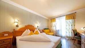A hotel room with a large bed, a wooden nightstand, a desk, a chair, and a window with curtains. - Palmengarten Hotel Gstv R (Lagundo)