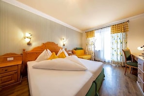 A hotel room with a large bed, a wooden nightstand, a desk, a chair, and a window with curtains. - Palmengarten Hotel Gstv R (Lagundo)