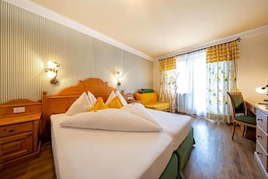 Una habitación de hotel con una cama grande, una mesita de noche de madera, un escritorio, una silla y una ventana con cortinas.