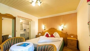 A hotel room with a bed, two chairs, a table, a mirror, and a wooden headboard. - Palmengarten Hotel Gstv R (Lagundo)