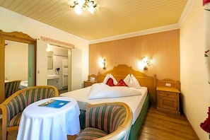 A hotel room with a bed, two chairs, a table, a mirror, and a wooden headboard. - Palmengarten Hotel Gstv R (Lagundo)