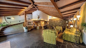 A spacious interior with a stone floor, wooden beams, a staircase, and a stone wall with a mounted animal head. - Palmengarten Hotel Gstv R (Lagundo)