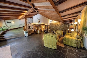 A spacious interior with a stone floor, wooden beams, a staircase, and a stone wall with a mounted animal head. - Palmengarten Hotel Gstv R (Lagundo)