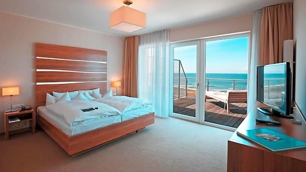 Habitación de hotel con cama, escritorio con computadora, televisión y vista al océano a través de una puerta corrediza.