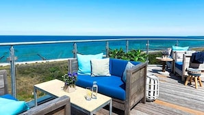 Una terraza de madera con un sofá y sillas, con vista a la playa.