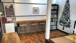 Et værelse med trægulv, hvid væg med et indrammet billede, en lille bar med barstole og et juletræ.