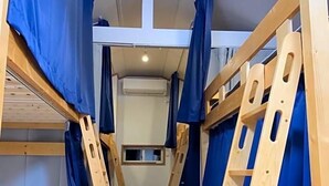 Et aflangt værelse med køjesenge og en stige, et lille vindue og en loftlampe.