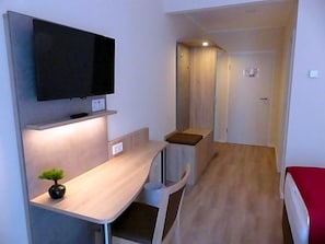 A compact room with a flat-screen TV mounted on the wall, a small table with a plant, and a bed with a red cover. - Ladiges Gasthof (Holm)
