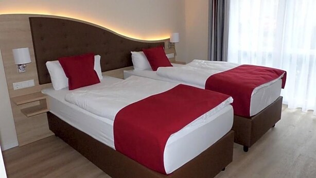 A hotel room with two beds, each with a red bedspread, a wooden headboard, and a bedside table with a lamp. - Ladiges Gasthof (Holm)