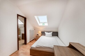 A small, well-lit bedroom with a skylight, a bedside table with a lamp, and a wooden headboard. - Hotel Glas Schwarzwald (Fluorn)