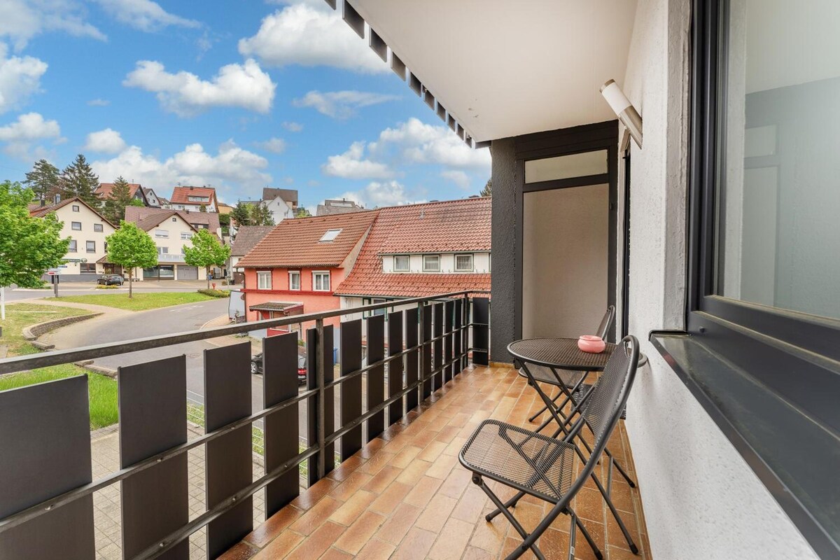 A balcony with a table and chairs, a view of the street, and a building in the background.