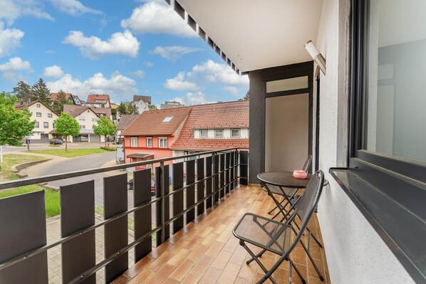 A balcony with a table and chairs, a view of the street, and a building in the background. - Hotel Glas Schwarzwald (Fluorn)