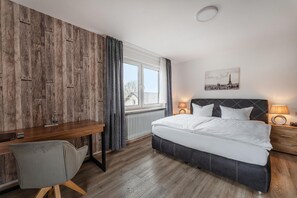 A hotel room with a wooden wall, a bed with white bedding, a desk with a chair, and a window with curtains. - Hotel Glas Schwarzwald (Fluorn)