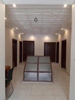 Une chambre d’hôtel dotée d’un espace salon central, de plusieurs portes et d’un sol carrelé.