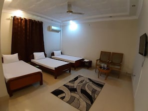 Une chambre d’hôtel avec deux lits simples, une petite table, une chaise, un ventilateur de plafond et un téléviseur.