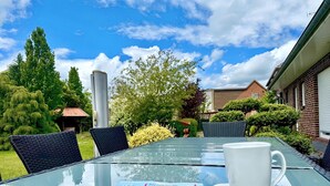 A glass-top table with a white mug and a menu, surrounded by wicker chairs, set outdoors with a clear sky and greenery in the background. - Ferienhaus Am Gla Ck (Bad Zwischenahn)