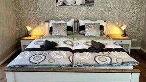 A double bed with a patterned bedspread, two bedside tables with lamps, and a wall-mounted picture of flowers. - Ferienhaus Am Gla Ck (Bad Zwischenahn)