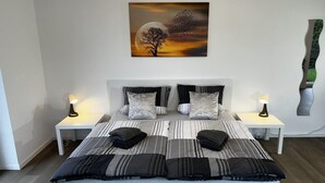 A modern bedroom with a large bed, two bedside tables, and a wall-mounted painting. - Ferienhaus Am Gla Ck (Bad Zwischenahn)