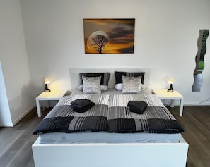 A modern bedroom with a large bed, two bedside tables, and a wall-mounted painting. - Ferienhaus Am Gla Ck (Bad Zwischenahn)