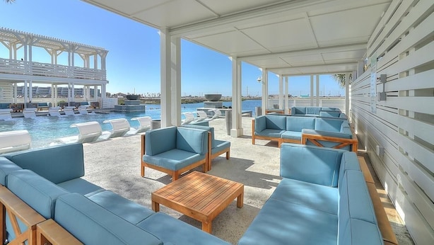 A covered outdoor seating area with lounge chairs and sofas, a pool, and a view of the sea. - Walking On Sunshine 246 Lak (Port Aransas)