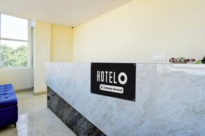 A hotel reception desk with a marble counter, a sign indicating it's a company-serviced hotel, and a window with a view of trees. - Hotel O Bolligudem (Hyderabad)