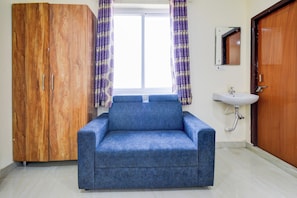 Une pièce avec un canapé bleu, une armoire en bois, une fenêtre avec des rideaux violets et un lavabo.