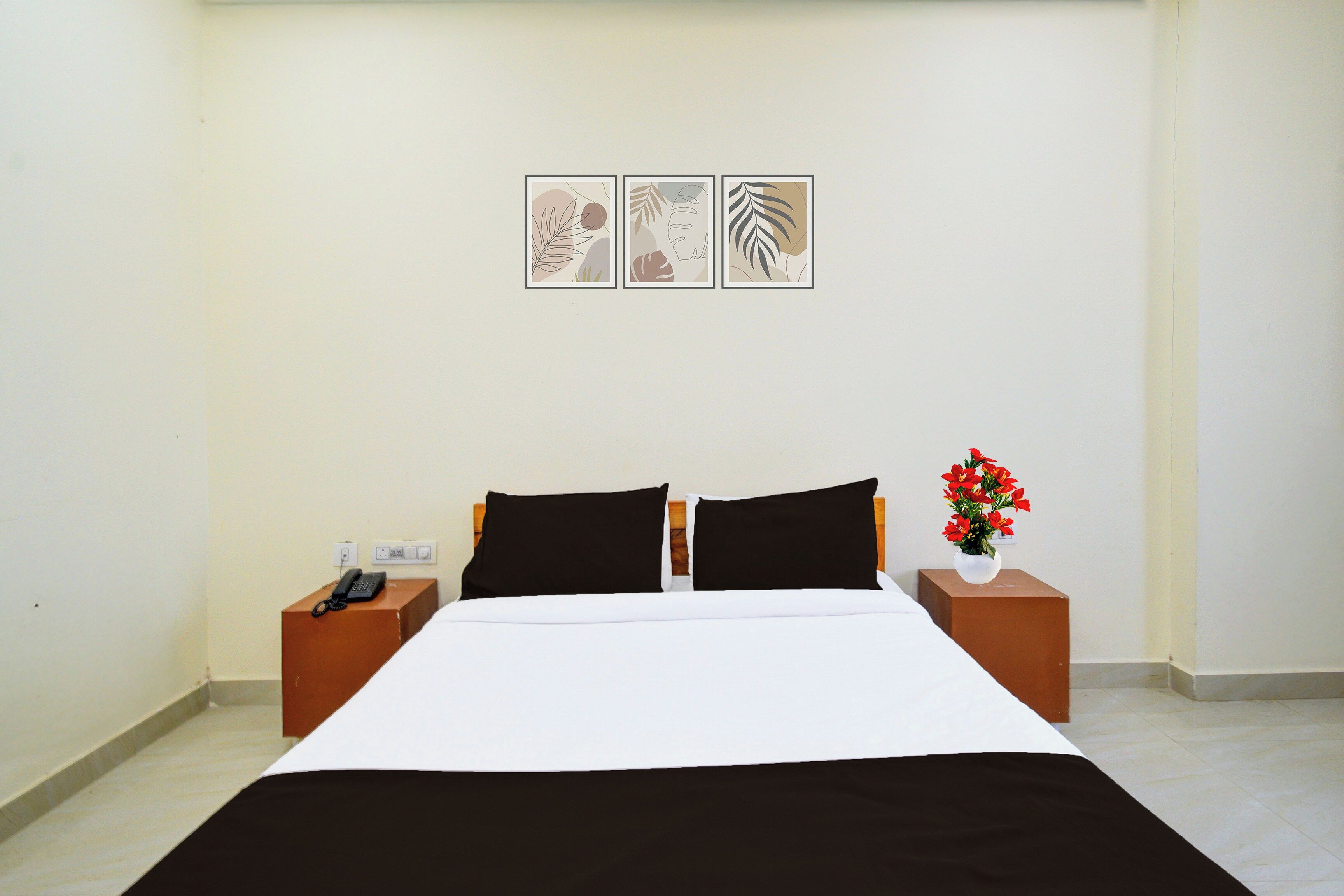 Una camera d'albergo con un letto, due comodini, un telefono e un vaso con fiori.