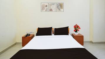 Una camera d'albergo con un letto, due comodini, un telefono e un vaso con fiori.