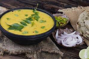 Un tazón de sopa adornado con hierbas, acompañado de cebolla en rodajas y media lima sobre una mesa de madera rústica.