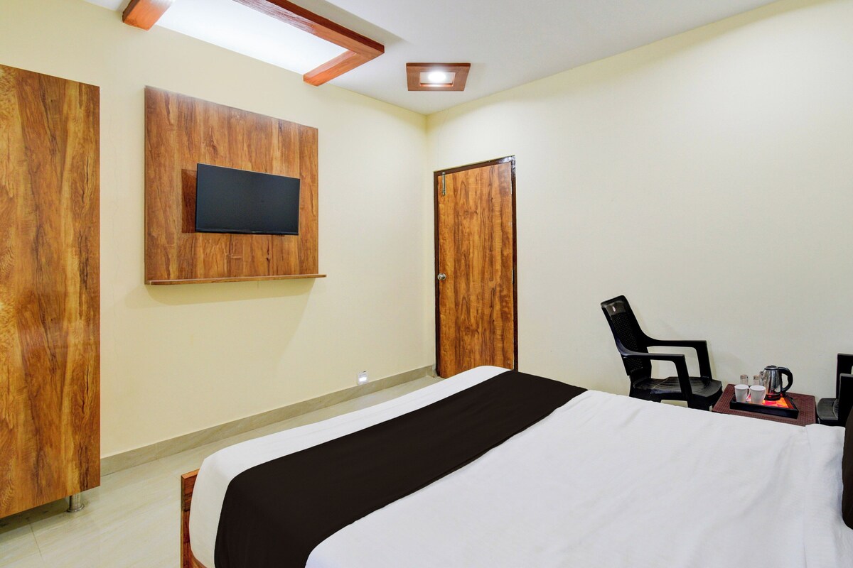 Une chambre d’hôtel avec un lit, un téléviseur fixé au mur, une armoire et une chaise sur laquelle se trouve un plateau avec divers objets.