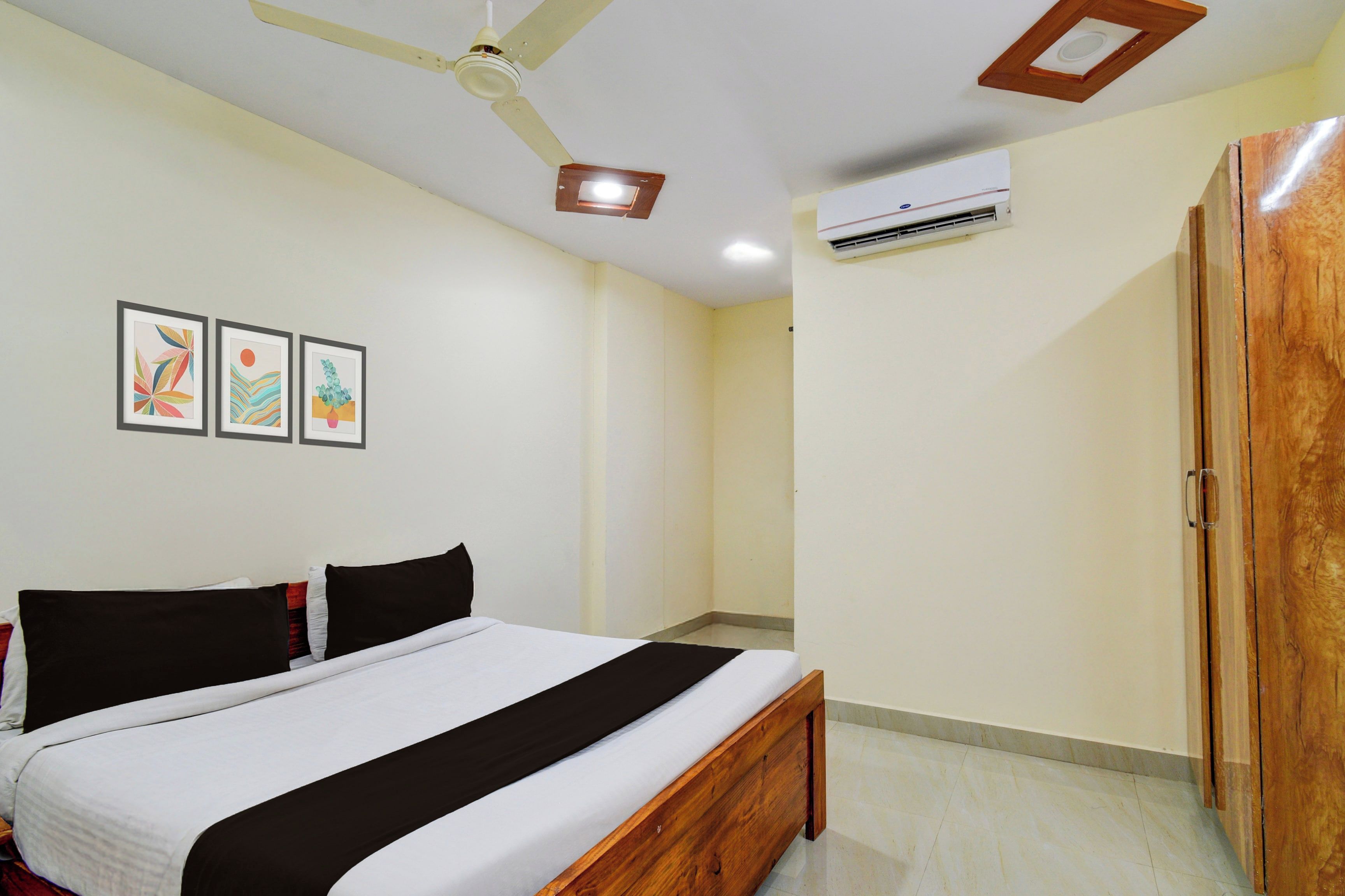 Un dormitorio con una cama, ventilador de techo, unidad de aire acondicionado y cuadros en la pared.