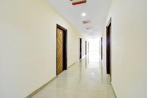 Un pasillo largo y estrecho con piso pulido, puertas a ambos lados e iluminación empotrada en el techo.