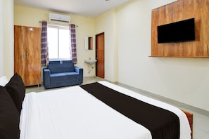 Une chambre d’hôtel avec un lit, un canap é bleu, un lavabo, un appareil de climatisation et un téléviseur fixé au mur.