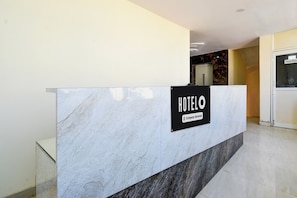 Un comptoir d’accueil d’hôtel, doté d’un plan de marbre et d’une enseigne indiquant qu’il s’agit d’un hôtel proposant des services aux entreprises.