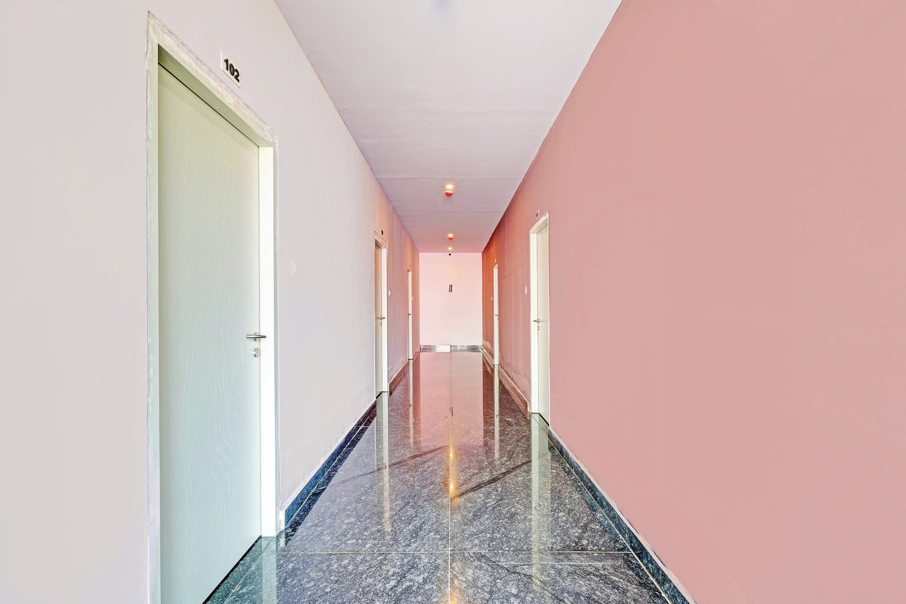 A corridor with doors on both sides, a tiled floor, and a ceiling with recessed lighting.