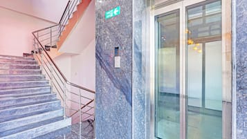 A staircase with metal railings leading to a fire exit sign on a marble wall.