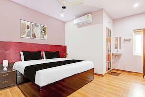 A bedroom with a bed, bedside table, lamp, air conditioning unit, and a bathroom with a sink and mirror. - OYO Hotel O Ramarvapadu (Vijayawada)