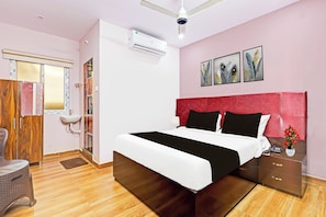 A bedroom with a bed, a bedside table, a mirror, a wall-mounted air conditioner, and a window with blinds. - OYO Hotel O Ramarvapadu (Vijayawada)