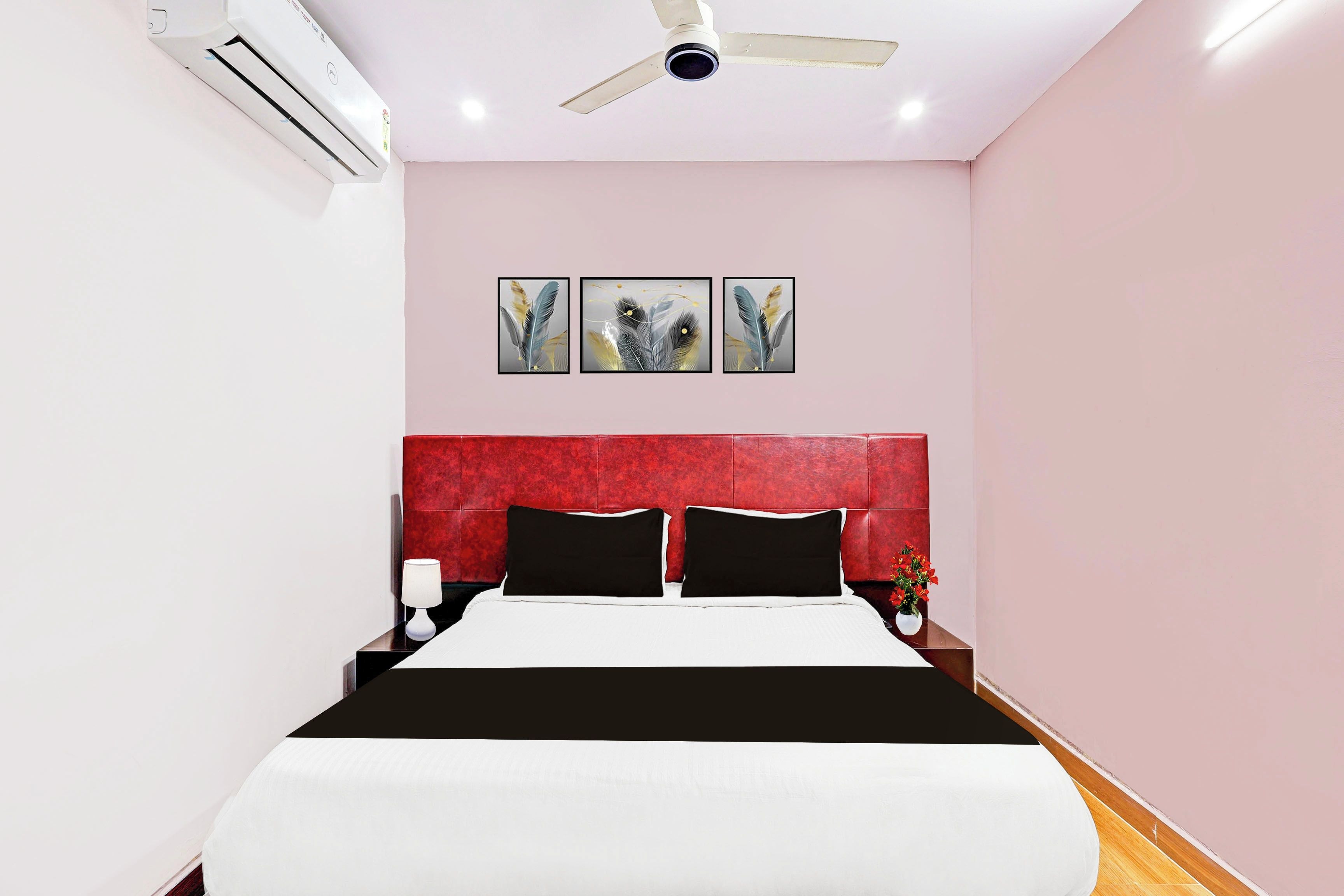 A hotel room with a bed, a red headboard, a ceiling fan, and three wall-mounted artworks.