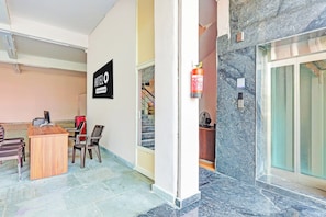 A hotel reception area with a desk, chairs, a fire extinguisher, and a staircase. - OYO Hotel O Ramarvapadu (Vijayawada)