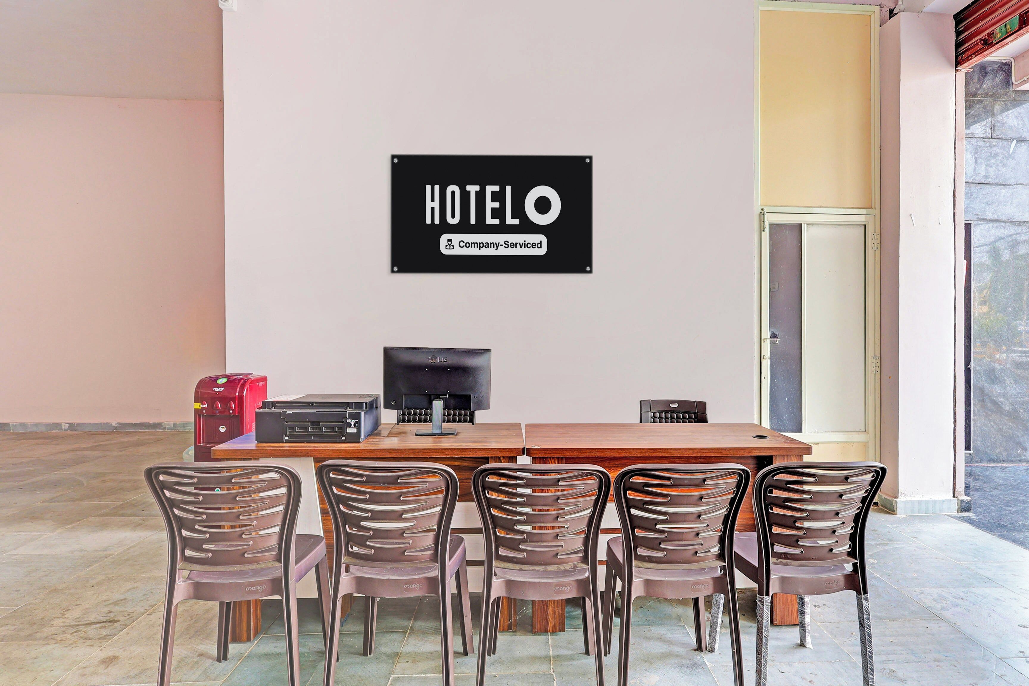 A hotel room with a wooden table, four chairs, a television, and a sign indicating the room is company-serviced.
