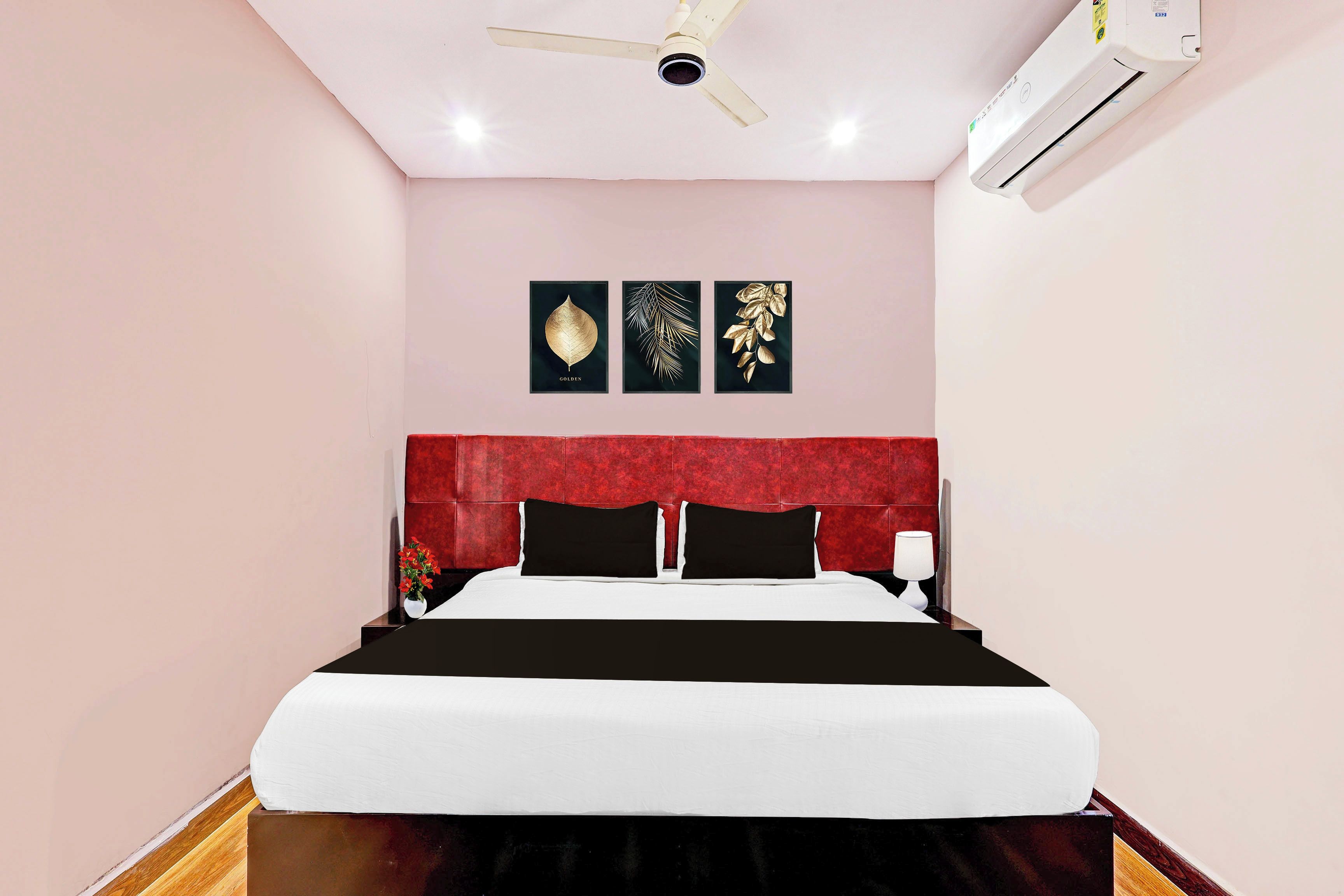 A hotel room with a bed, a red headboard, and three framed leaf artworks on the wall.