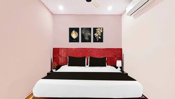 A hotel room with a bed, a red headboard, and three framed leaf artworks on the wall.