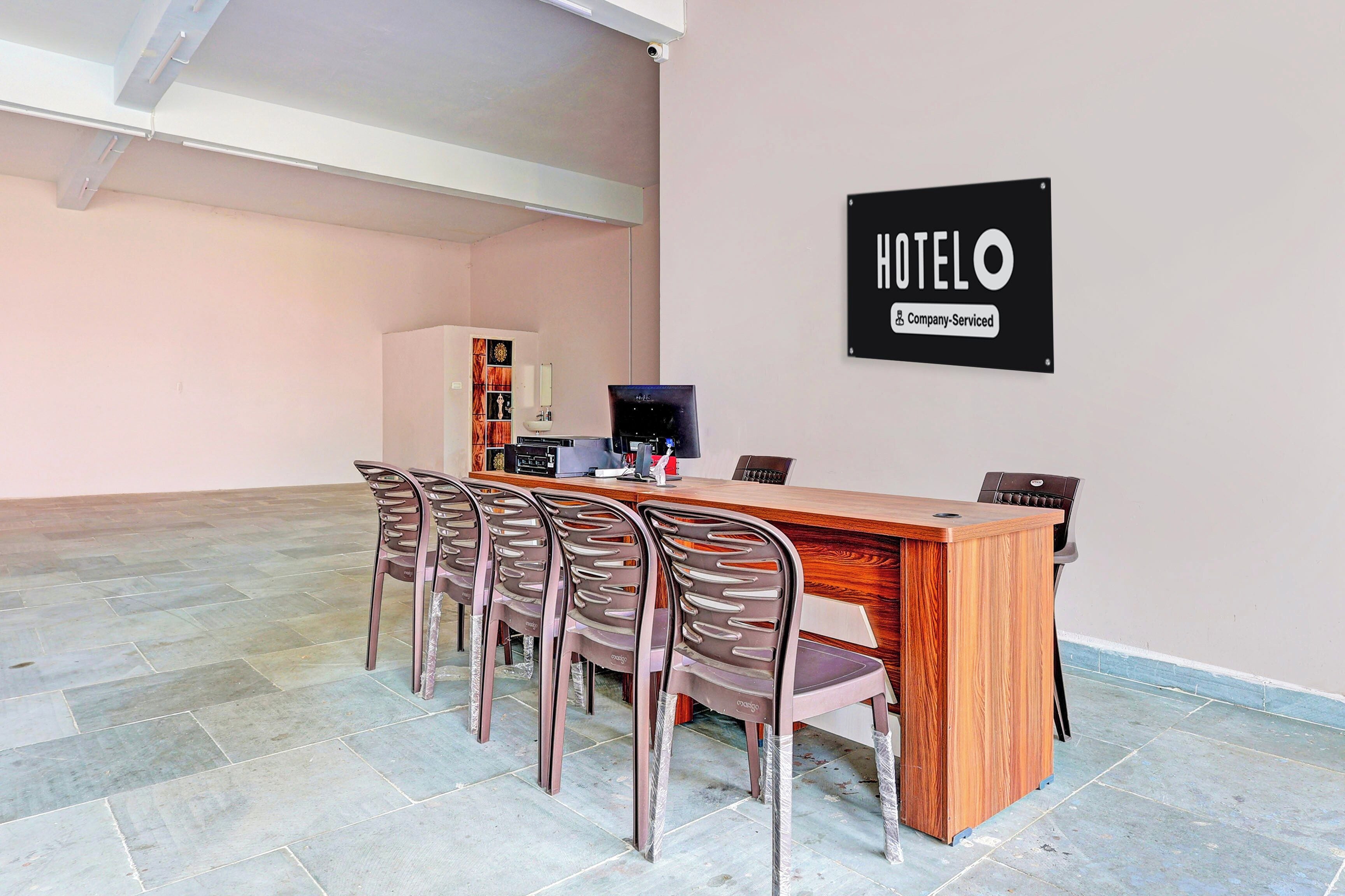 A hotel reception area with a wooden desk, a computer, and a sign indicating the hotel is company-serviced.