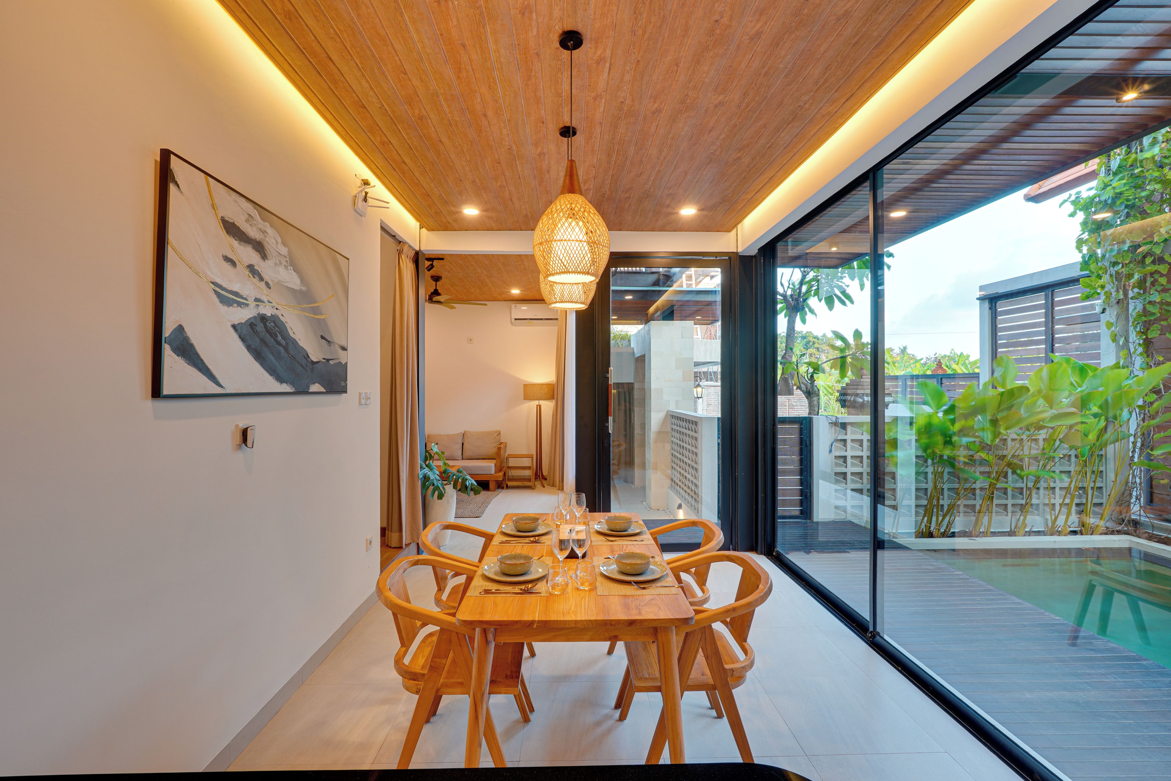 A dining area with a wooden table and chairs, a hanging light fixture, and a view of the outdoors.