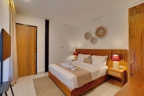 A hotel room with a wooden bed, a TV, a bedside table with a lamp, and decorative wall art. - Villa Tajung - Umalas (Badung)