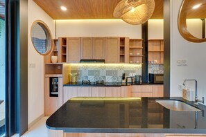 A modern kitchen with wooden cabinets, a black countertop, and a built-in stove. - Villa Tajung - Umalas (Badung)