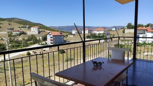 Un balcón con mesa y sillas, con vistas a una zona residencial con casas y colinas.